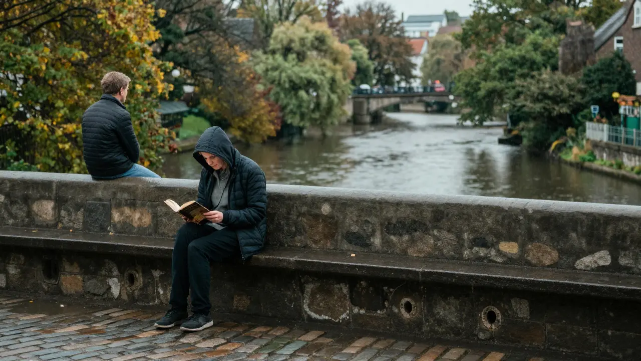 A solitary reader on a rainy Bristol bridge, another person pausing nearby in quiet mutual presence.